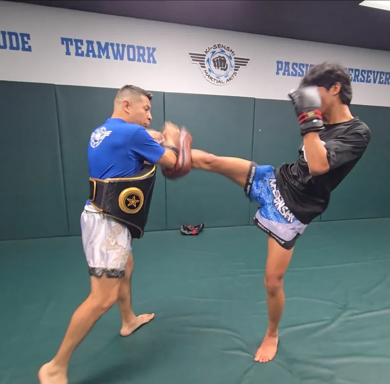 A martial arts student performing a high kick on a focus pad held by an instructor in Chandler.